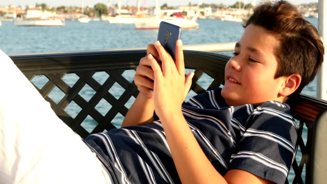 Niño-en-la-cubierta-del-yate-usando-el-teléfono-inteligente