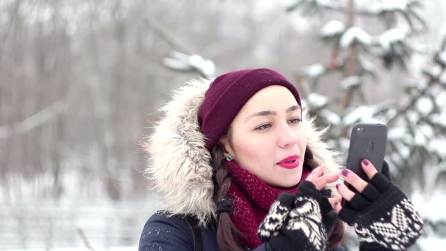 Schöne-junge-Mädchen-flippt-durch-soziale-Netzwerke-in-ihrem-Smartphone-beim-Gehen-in-einem-Winterpark.