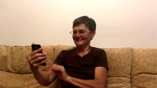 Attractive-adult-woman-makes-a-video-call-on-her-smartphone,-sitting-on-a-sofa-at-home.