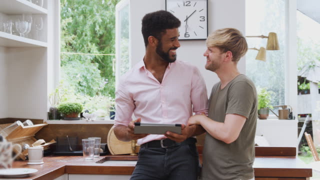 Pareja-gay-masculina-usando-tableta-digital-en-casa-en-la-cocina-juntos