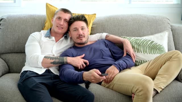 Gay-couple-relaxing-on-couch-watching-tv.-Trying-to-find-the-right-channel.