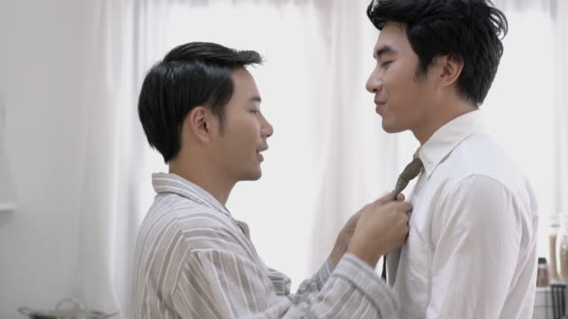 Asian-couple-gay-helping-tie-a-necktie-and-dress-to-work-in-morning-at-home.-Gay-boy-happy-emotion-and-hug-love-anniversary-together.-Concept-of-lifestyle,-family,-gay-and-bisexual.