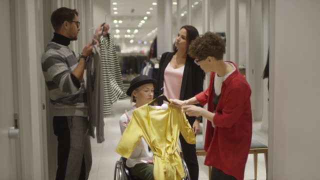 Frau-im-Rollstuhl-Einkaufen-für-Kleidung-mit-Hilfe-von-Freunden