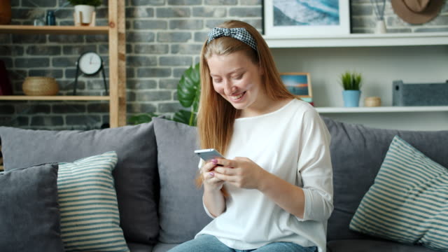 Schöne-blonde-Mädchen-mit-Smartphone-und-lachen-entspannend-auf-der-Couch-zu-Hause