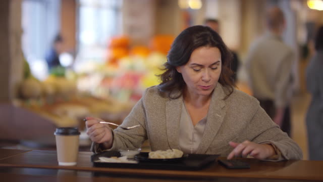 Mujer-usando-el-teléfono-y-comiendo-el-almuerzo-en-la-mesa-en-el-mercado-de-alimentos