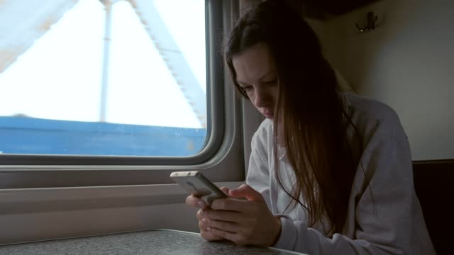 Tired-young-woman-in-train-looking-in-mobile-phone.