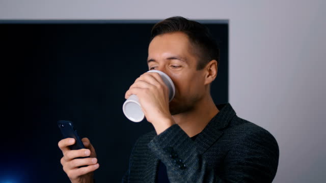 Selbstbewusster-Geschäftsmann-trinkt-Kaffee-und-benutzt-ein-Smartphone-im-Büro-während-einer-Kaffeepause