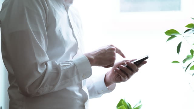 Body-of-Man-in-White-Dress-Shirt-Pressing-Cell-Phone-Buttons