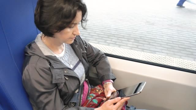 Mujer-caucásica-montando-en-un-tren-sentado-por-la-ventana-mirando-la-pantalla-de-la-tableta