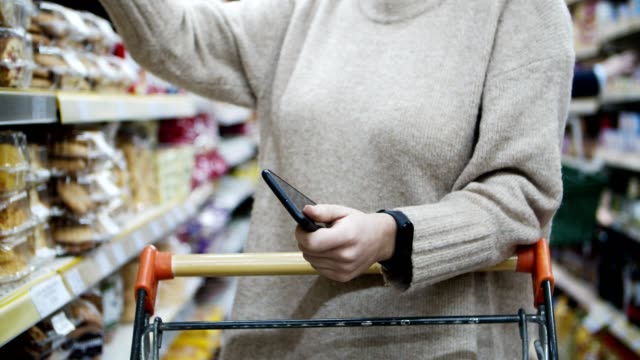 Mujer-sosteniendo-teléfono-inteligente-y-eligiendo-bienes