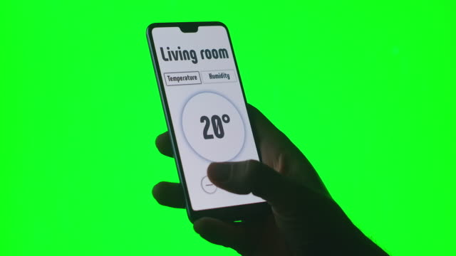 Auf-dem-grünen-Hintergrund-des-Chromakeys-steuert-ein-Mann-die-Temperatur--und-Alarmsysteme-über-eine-App-auf-seinem-Handy