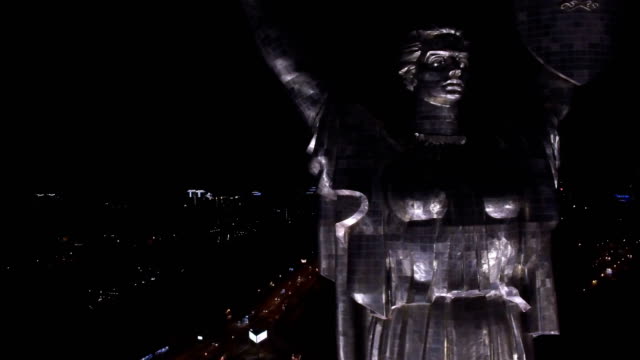 Vista-aérea-de-la-madre-patria-en-la-noche-con-las-luces-iluminadas,-el-monumento-se-encuentra-en-los-bancos-del-río-Dnieper.-Kiev,-Ucrania.-Rodada-en-4K-UHD