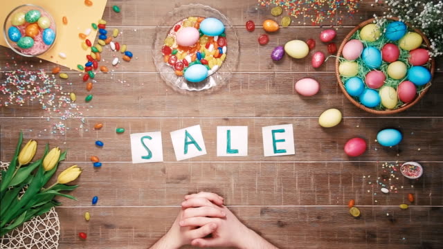 Man-puts-word-Sale-on-table-decorated-with-easter-eggs.-Top-view