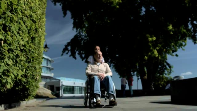 Pleasant-volunteer-pushing-a-wheelchair-of-an-aged-man