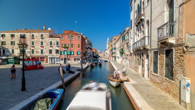 A-view-of-Venice-timelapse:-canal,-bridge,-boats-and-an-old-tower-in-the-background