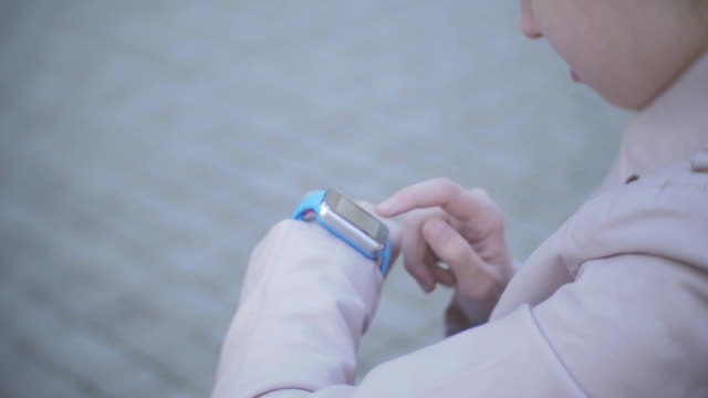 Closeup-tilt-up-shot-of-mixed-race-student-girl-using-smartwatch-and-smiling-near-univercity-at-street