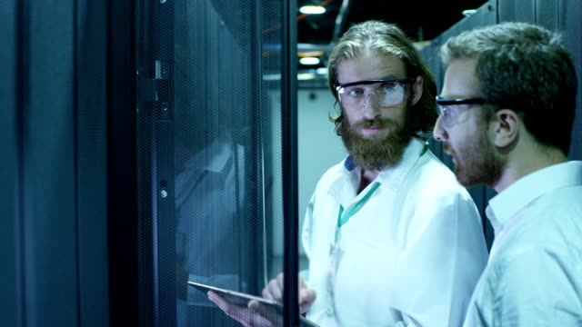 Dos-ingenieros-informáticos-están-trabajando-en-un-centro-de-datos.-Ellos-están-discutiendo-su-trabajo.-Tiro-de-cámara-RED-EPIC-cine-en-cámara-lenta.