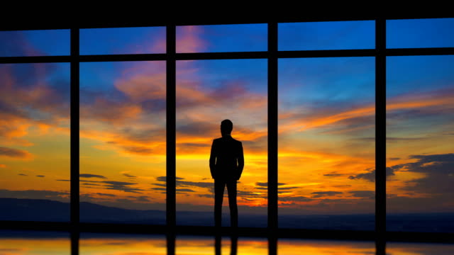 Der-Mann-steht-in-der-Nähe-von-Fenstern-auf-den-Sonnenaufgang-Hintergrund.-Zeitraffer