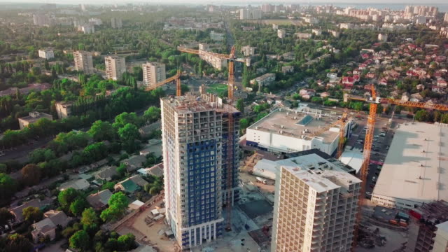 Aerial-drone-shot.-Construction-of-high-rise-buildings-in-the-developing-area-of-a-large-city.-Sunset-shot.-Small-buildings,-construction-cranes-and-many-houses-under-construction.-wide-shot