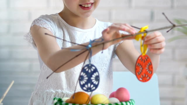 Smiling-girl-preparing-Easter-decoration,-hanging-toy-eggs-on-tree-branches,-eve
