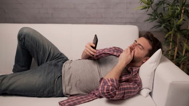 Sleepy-man-using-smartphone-on-the-couch