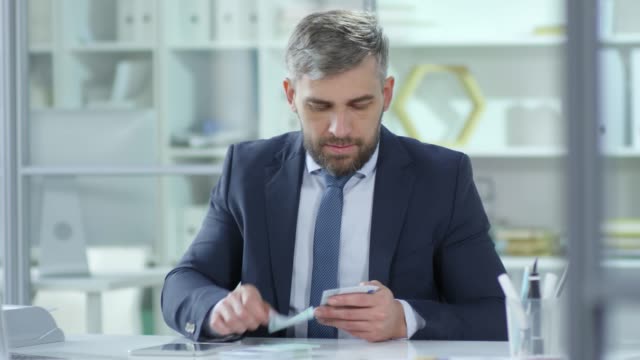 Businessman-Counting-Money-and-Using-Digital-Tablet