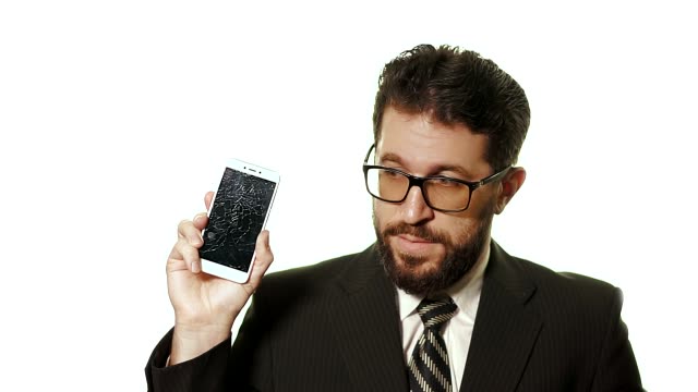 Das-Konzept-eines-kaputten-Gadgets.-Bärtiger-Geschäftsmann-in-einer-Brille,-die-kaputten-Smartphone-Bildschirm-zeigt,-er-steht-unter-Schock-und-weiß-nicht,-was.