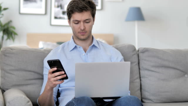 Hübsche-junge-Mann-nutzt-Smartphone-zur-Arbeit,-sitzt-auf-Couch
