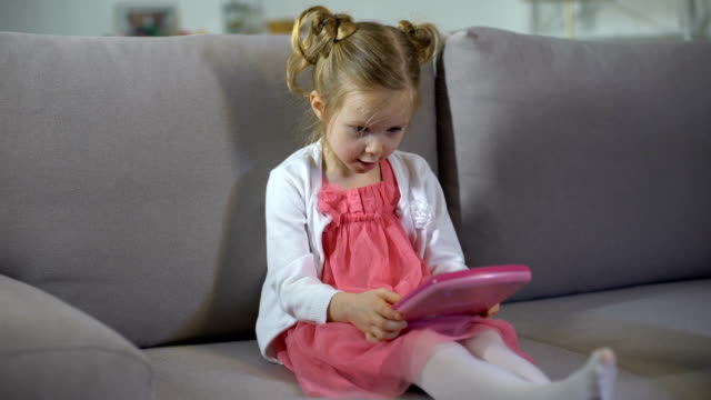 Lustiges-Mädchen-auf-dem-Sofa-sitzen-und-auf-rosa-Spielzeug-Tablet-pädagogische-App-spielen