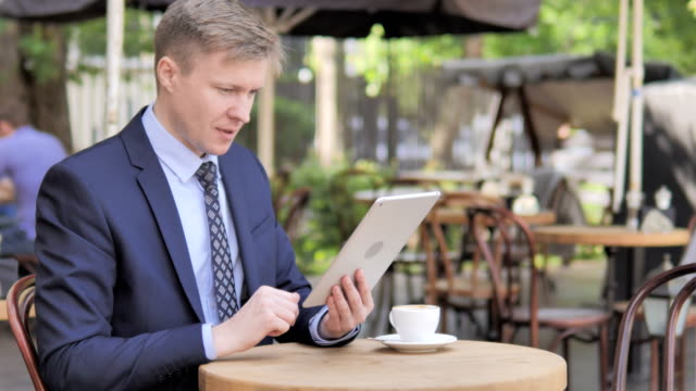 Businessman-Celebrating-Win-on-Tablet,-Sitting-in-Outdoor-Cafe
