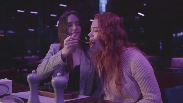 Pretty-young-girl-feeding-her-girlfriend-resting-in-an-expensive-restaurant.