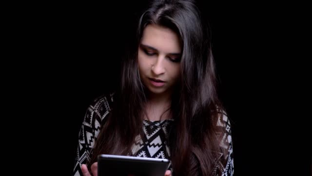 Nahaufnahme-von-jungen-hübschen-kaukasischen-weiblichen-Texten-auf-dem-Tablet-dann-blick-auf-die-Kamera-und-lächelnd-mit-Hintergrund-isoliert-auf-schwarz