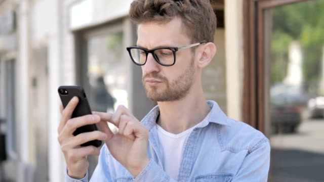 Lässiger-junger-Mann-mit-Smartphone-im-Freien