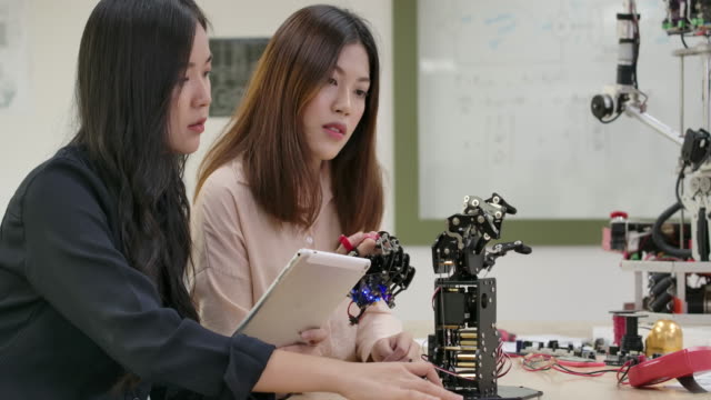 Team-von-talentierten-Ingenieuren,-die-innovative-Robotertechnologie-im-Labor-testen.-Zwei-asiatische-Weibchen-schafft-Bewegung-für-mechanische-Roboterhand.-Menschen-mit-Technologie--oder-Innovationskonzept.