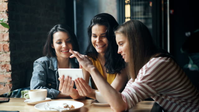 Joyful-girls-looking-at-smartphone-screen-swiping-smiling-having-fun-in-cafe