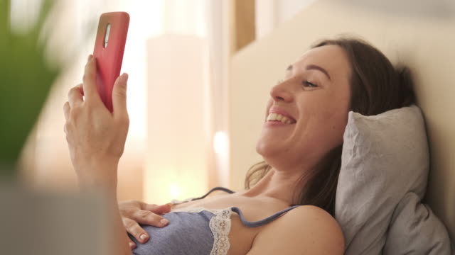 Excited-woman-video-chatting-using-mobile-phone-in-bed