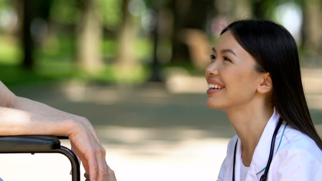 Lächelnde-Krankenschwester-kommuniziert-mit-Rentnerin-im-Rollstuhl-und-unterstützt-sie