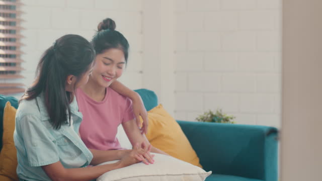 Young-Asian-Lesbian-couple-hug-and-kiss-lying-sofa-in-living-room-at-home.