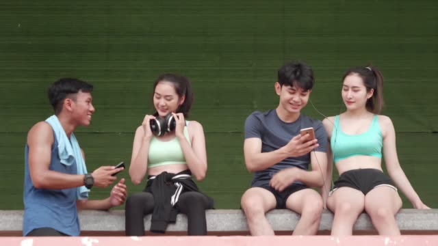 Asiatische-junge-Männer-und-Mädchen-Relexing-Übung-nach-Sport-läuft-Peple-verwenden-Smartphone-Play-App-Musik