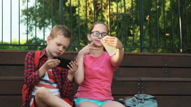 The-older-sister-and-brother-are-sitting-on-the-street,-looking-at-smartphones.