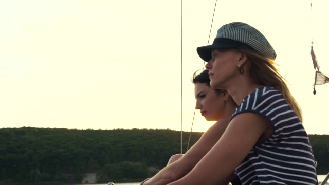 zwei-junge-Frauen-entspannen-auf-Segelboot-und-beobachten-Sonnenuntergang