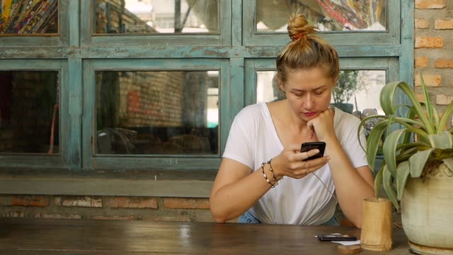 Pensive-girl-uses-a-smartphone,-writes-a-message,-chatting.-Woman-looking-for-information-in-the-phone-and-sad.-Sitting-in-restaurant-alone.-Breakfast-time.-Technology-and-entertainment-concept