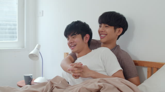 Schöne-asiatische-homosexuell-Paar-im-Bett-zu-Hause-sprechen.-Junge-asiatische-LGBTQ-+-Kerl-glücklich-entspannen-zusammen-verbringen-romantische-Zeit-nach-dem-Aufwachen-im-Schlafzimmer-im-modernen-Haus-im-Morgen-Konzept.
