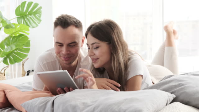 Couple-using-digital-tablet-lying-on-bed