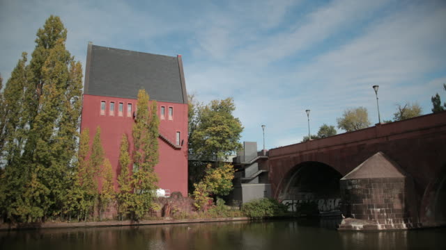 Schönes-rotes-Hochhaus-auf-der-gegenüberliegenden-Seite-des-Flusses,-eine-alte-Brücke-über-den-Teich.