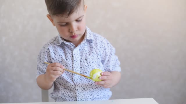 Un-niño-pinta-un-huevo-de-pascua-en-la-mesa-sobre-un-fondo-blanco.