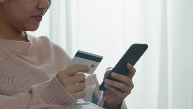 Nahaufnahme-Hand-der-asiatischen-Frau-hält-Smartphone-und-Kreditkarte-für-die-Zahlung-und-Online-Shopping-zu-Hause.-Glückliche-Frau-machen-Transaktion-mit-mobilen-Bank-Anwendung.-Online-Shopping-Konzept.