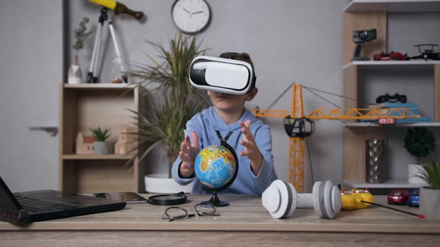 Atractivo-niño-concentrado-de-6-años-sentado-en-la-mesa-en-su-habitación-y-se-tachando-la-estructura-del-globo-usando-gafas-virtuales-especiales-en-3D