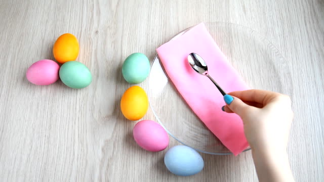 Hand-puts-a-teaspoon-next-to-colored-eggs-on-festive-Easter-table.
