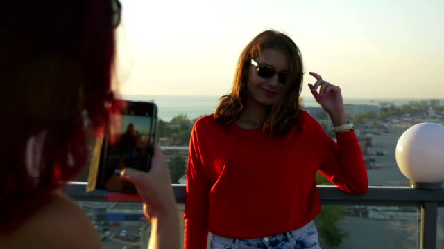 Two-girlfriends-taking-photos-with-smartphone-on-a-rooftop